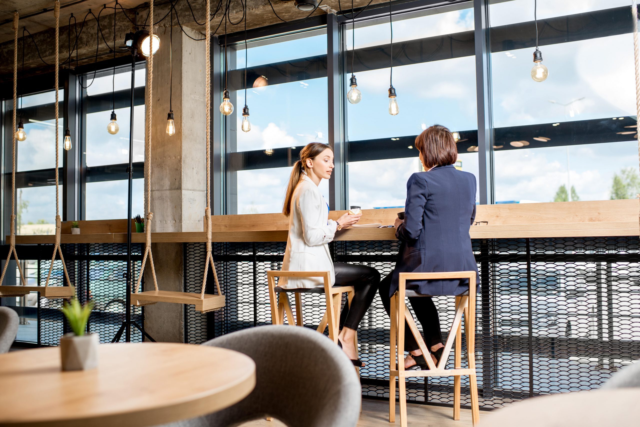 Two business women sitting during a coffee time near the window in the modern cafe interior